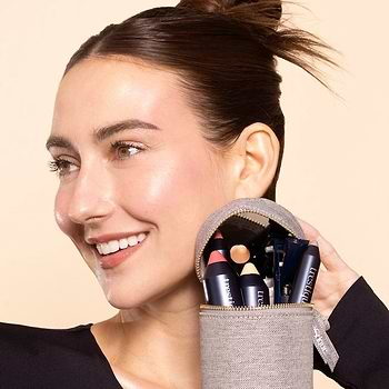 Smiling woman holding a zippered pouch filled with Trestique makeup products in travel beauty bag navy against a light background.