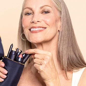 Smiling woman holding a pouch of Trestique cruelty-free makeup products, including lip, brow, and foundation sticks.