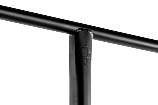 Close-up of the Ethic DTC Tenacity V2 steel oversized HIC stunt scooter T-bars in black, featuring a welded joint. The joint displays an embossed logo resembling a shield with letters inside. The white background highlights the lightweight design and craftsmanship, showcasing its high-quality steel construction by Ethic.