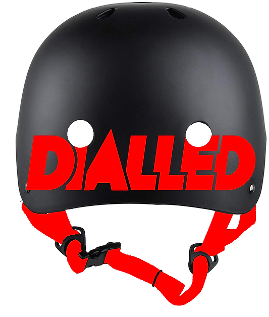 Introducing the Dialled Protection Adjustable Skate/Scooter Helmet in Black/Red: This helmet showcases a sleek black design with "DIALLED" prominently displayed in bold red letters across the front. It is constructed with a robust ABS shell to ensure safety and features red adjustable chin straps for a customizable fit, offering both style and protection effortlessly.