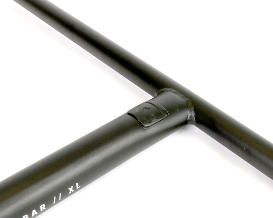 Close-up of a black metal T-joint, likely part of a handlebar crafted from Chromoly 4130 Steel, with visible welds. The size markings "XL" are clearly seen on one side, reminiscent of the design and durability of Root Industries' Steel Oversized SCS XL Stunt Scooter T-Bars in Black, measuring 710mm by 610mm.