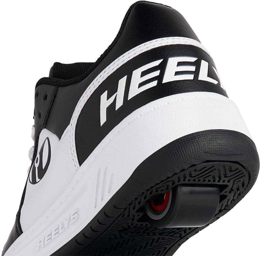 Close-up of the heel on Heelys Rezerve Low Boys Shoes in Black/White/White, showing the "Heelys" logo and a wheel with ABEC 5 bearings in the sole, designed to be beginner-friendly.