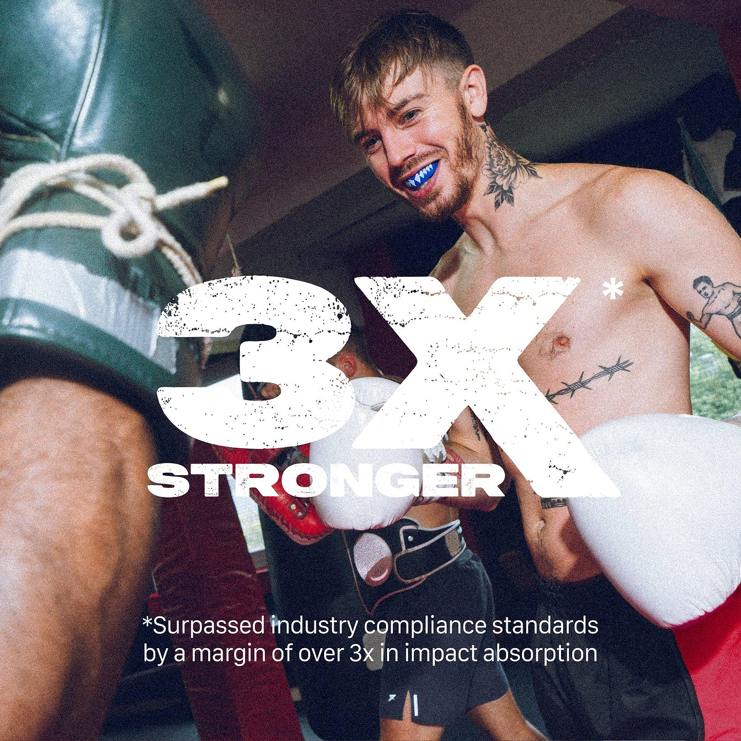 A tattooed male boxer in a gym smiles while sparring, wearing a blue Safejawz Extro Series Protection Mouthguard - Shark and white gloves. Bold text says “3X STRONGER,” noting it exceeds impact absorption standards.