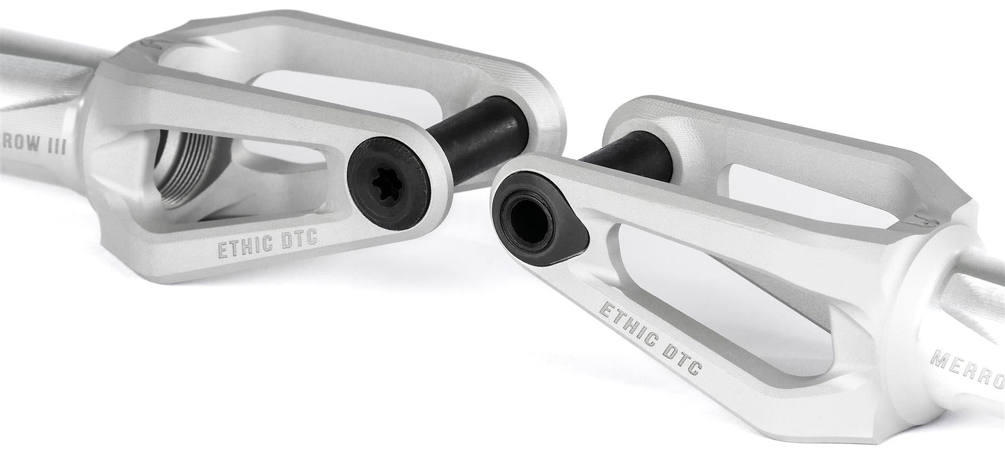 Close-up of two Ethic DTC Merrow V3 8/12STD SCS Stunt Scooter Forks by Ethic in a raw matte finish, featuring detailed cutouts and black hardware, displayed on a white background.