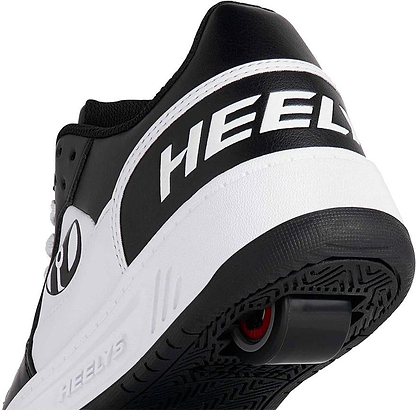 Close-up of the heel on Heelys Rezerve Low Boys Shoes in Black/White/White, showing the "Heelys" logo and a wheel with ABEC 5 bearings in the sole, designed to be beginner-friendly.