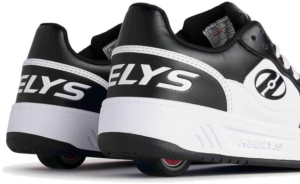 A close-up of Heelys Rezerve Low Boys Shoes in Black/White, featuring the Heelys brand on the heel, retractable wheels in the soles, and ABEC 5 bearings for smooth rolling.