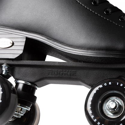 Close-up of the Rookie Classic 78 Quad Roller Skates - Black by Rookie, featuring part of the boot, metal plate, and two black wheels with white text. Laces and textured detailing showcase their classic style.