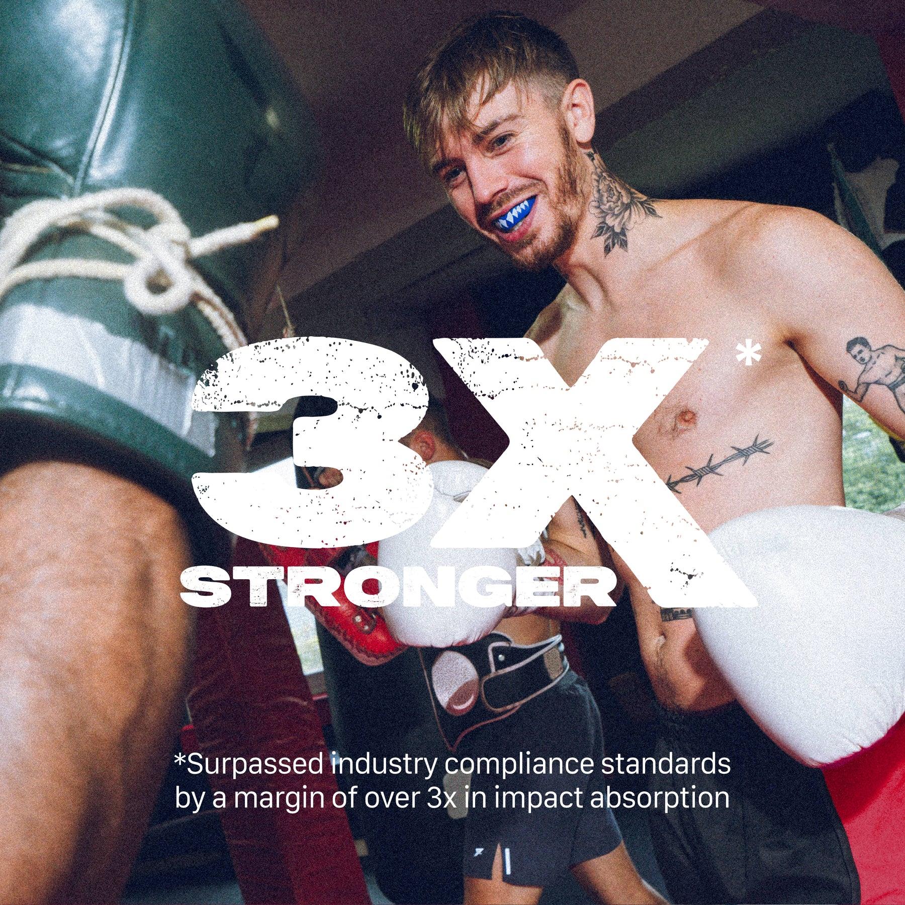 A tattooed male boxer in a gym smiles while sparring, wearing a blue Safejawz Extro Series Protection Mouthguard - Shark and white gloves. Bold text says “3X STRONGER,” noting it exceeds impact absorption standards.