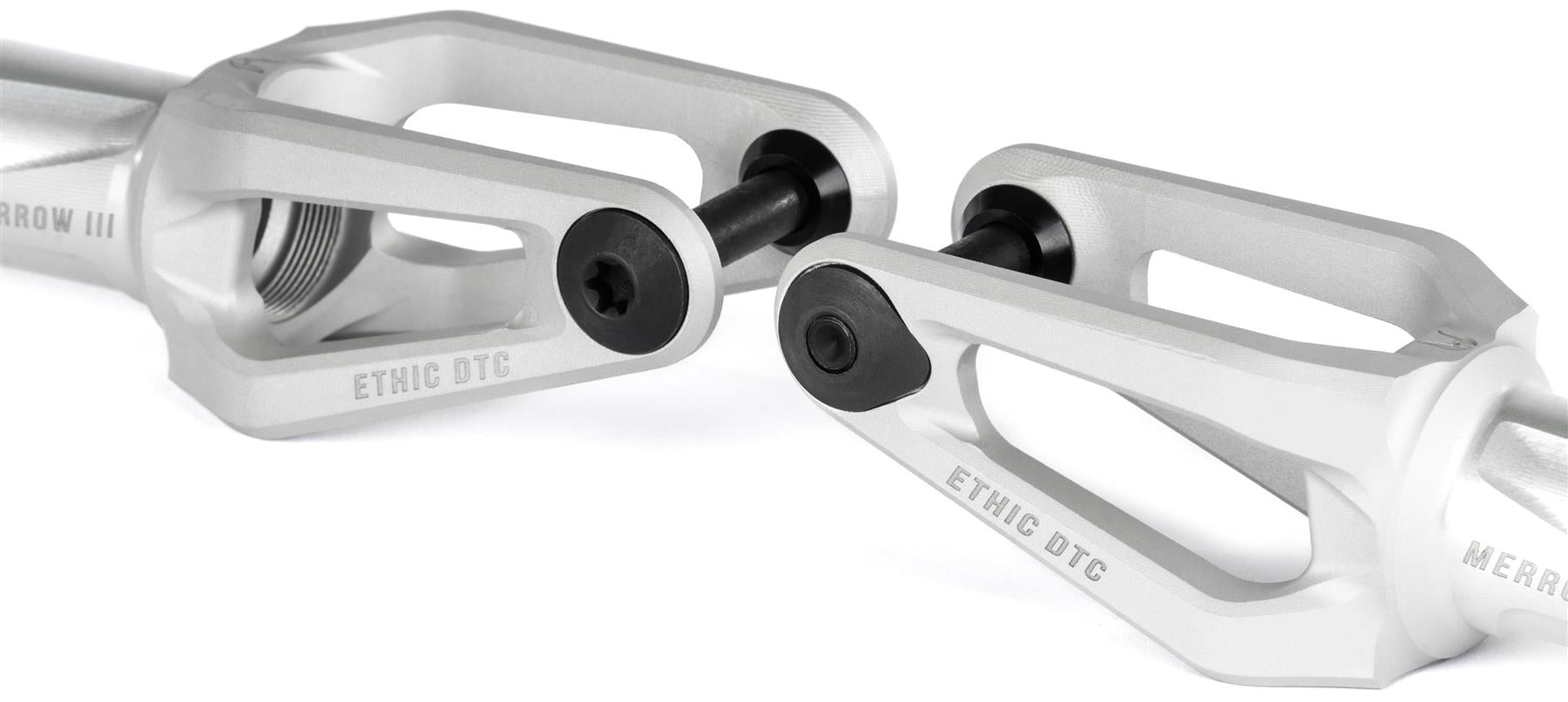 Close-up of two Ethic DTC Merrow V3 8/12STD IHC Stunt Scooter Forks in raw finish, featuring black bolts, "ETHIC DTC" engraving, and a modern lightweight design with cutouts. Brand: Ethic.