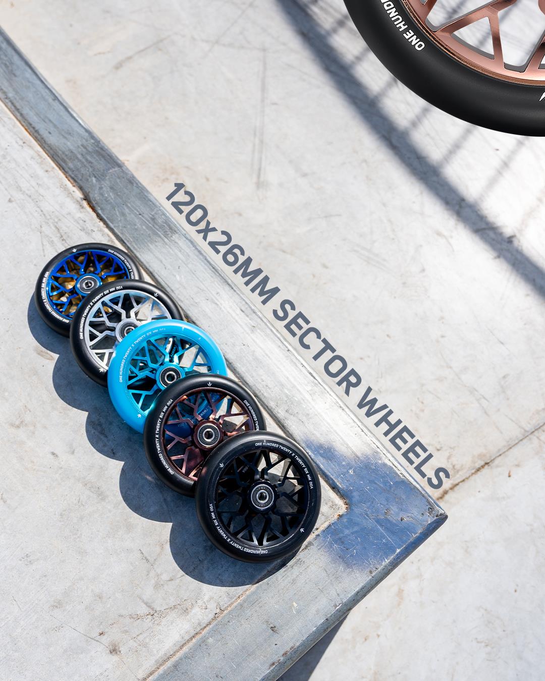 Five Blunt Envy stunt scooter wheels, including the Blunt Envy Sector 120mm Stunt Scooter Wheel - Black, are lined up diagonally on concrete near a skatepark ramp. "120x26MM SECTOR WHEELS" is written on the ground; a bronze wheel is partially visible.
