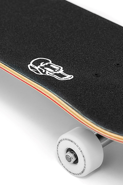 Close-up of the Enuff Three Tier Reloaded Black Complete Skateboard (8.0" x 32.0") by Enuff, featuring black grip tape with a white skull near the edge, exposed wooden layers underneath, and a visible white wheel at the bottom right.