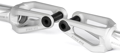 Close-up of two Ethic DTC Merrow V3 8/12STD SCS Stunt Scooter Forks by Ethic in a raw matte finish, featuring detailed cutouts and black hardware, displayed on a white background.