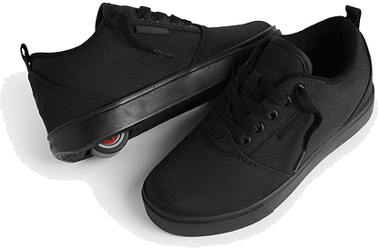 A pair of Heelys Pro 20 Boys Shoes - Triple Black Canvas, with one shoe on its side displaying a retractable wheel in the heel, showing they are kids' roller shoes by Heelys.