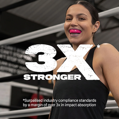 A woman in athletic wear smiles in a gym with boxing rings, wearing the Safejawz Intro Series Protection Mouthguard - Pink for jaw stability. Bold text reads "3X STRONGER" with a note on impact absorption. Brand: Safejawz.