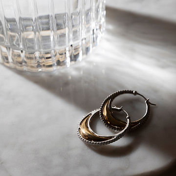 Gold hoop earrings on a marble surface with a glass object in the background