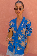 Modella con il Cardigan Blue Eye dalla vestibilità comoda e motivo di occhi contro una parete rosa.