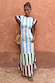Blue Stripe Alena Midi Dress with tiered multi-coloured stripes and ruffled sleeves against a terracotta wall.