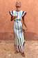 Blue Stripe Alena Midi Dress with multi-coloured tiered stripes and frill sleeves against a textured wall.