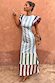 Blue Stripe Alena Midi Dress featuring ruffled sleeves and a tiered striped hem, posed against a terracotta wall.