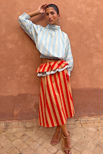 Blue Stripe Batwing Blouse paired with a red striped ruffled skirt against a terracotta wall.