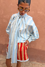 Blue Stripe Batwing Blouse with voluminous sleeves and a high tie neck, styled with red and tan striped shorts.
