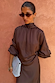 Blusa Chocolate Tie Neck con maniche ampie e collo alto, abbinata a occhiali da sole e clutch azzurra.