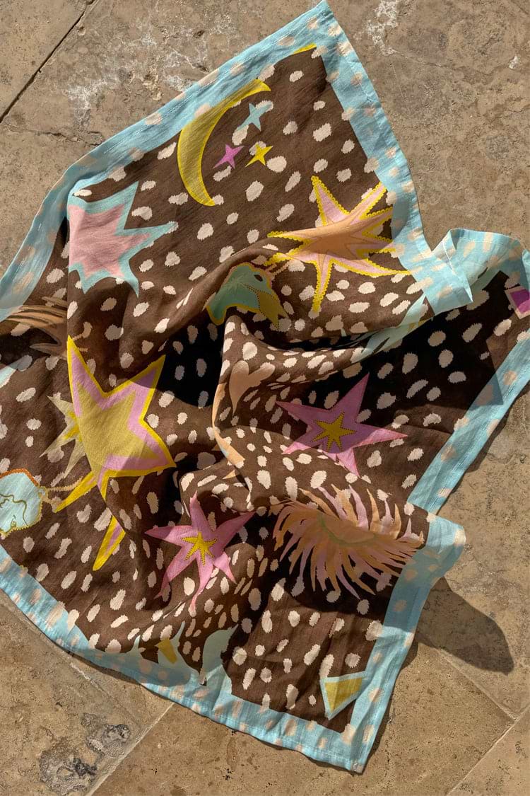 Bandana Star Fawn marrone con stampa maculata, stelle e lune colorate e bordo celeste su pietra.