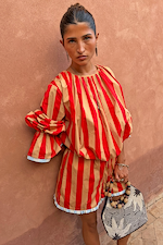 Model wears the red and camel Tomato Stripe Blouse with voluminous sleeves against a textured wall.