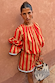 Model wears the red and camel Tomato Stripe Blouse with voluminous sleeves against a textured wall.
