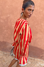Red and camel Tomato Stripe Blouse with voluminous sleeves and flared cuffs against a warm wall.