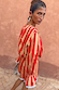 Red and camel Tomato Stripe Blouse with voluminous sleeves and flared cuffs against a warm wall.