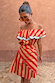 Model wearing the Tomato Stripe Mini Dress with red and camel stripes and a ruffled off-the-shoulder neckline