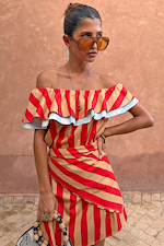 Red, tan and light blue Tomato Stripe Scarf styled as a multi-wear ruffled top against a terracotta wall.