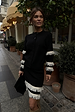 model is wearing a black cardigan and skirt with cream fringe detailing on the sleeves and skirt hem