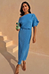 Abito Tilly plissé blu con dettagli dorati, indossato da una modella alta 170 cm in taglia M con pochette.