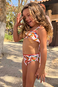 Bambina con il bikini a stampa banane multicolore, top a fascia con volant e slip coordinati.