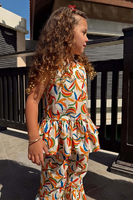 Bambina con top peplum in cotone crema e pantaloni svasati con stampa a banane multicolore.