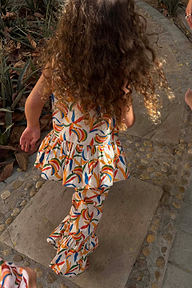 Set coordinato in cotone crema con stampa a banane, top peplo e pantaloni svasati su una bambina all'aperto.