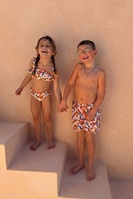Shorts da mare panna con stampa a banane multicolore, indossati da un bambino che ride sulle scale.