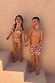 Boy's cream banana print swim shorts featuring multi-coloured graphics, worn by a child laughing on stairs.