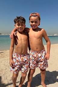 Shorts da mare da bambino con stampa a banane multicolore, indossati da due bambini su una spiaggia soleggiata.
