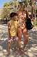 Boy wearing multi-coloured Banana Print Swim Shorts and yellow t-shirt with woman in matching swimsuit on a beach.