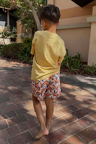 Bambino con shorts da mare panna con stampa banane multicolore e t-shirt gialla all'aperto.