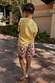 Boy wearing cream multi-coloured banana print swim shorts and a yellow t-shirt outdoors.