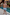 Thumbnail for Blue Starburst Swim Shorts with vibrant sun and star motifs, worn by a boy standing by a swimming pool.