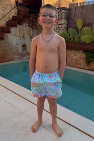 Blue Starburst Swim Shorts with vibrant sun and star motifs, worn by a boy standing by a swimming pool.