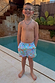 Blue Starburst Swim Shorts with vibrant sun and star motifs, worn by a boy standing by a swimming pool.