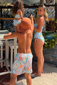 Boy wearing Starburst Swim Shorts in light blue with a sun and star print outdoors with family.