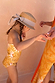 Girl's Yellow Sun Swimsuit with sun print and frill detailing, worn with a straw hat against a peach wall.