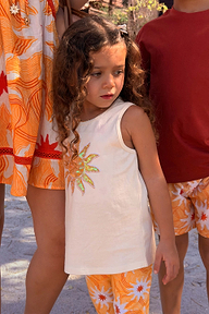 Girl wearing a cream cotton vest with a sequined soleil sun motif and yellow sun print trousers.